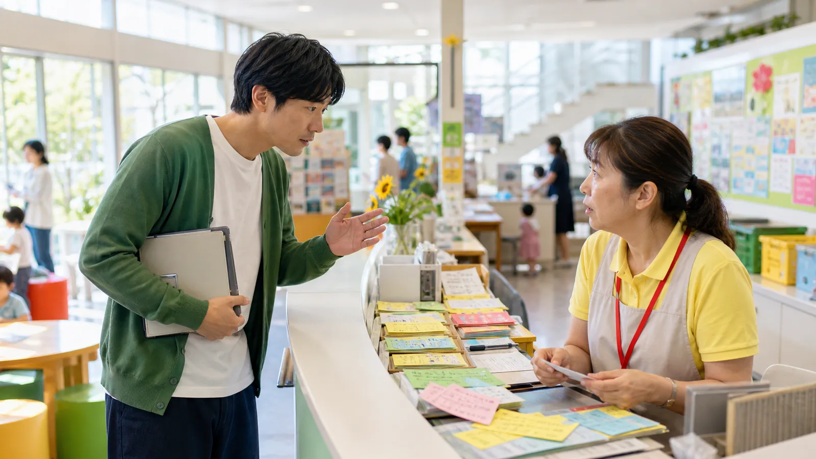 明るい地域施設で、学習ノートを抱えたエンジニアが、受付作業に追われる職員へ声をかけようとする様子